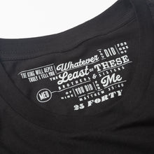 Load image into Gallery viewer, Close up of Plain black t shirt with Matthew 25:40 printed as the tag