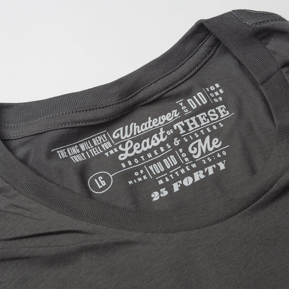 Close up of Matthew 25:40 printed as the tag on a charcoal gray t shirt