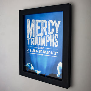 Mercy triumphs over judgement, James 2:13, printed on dramatic blue sky in black frame.