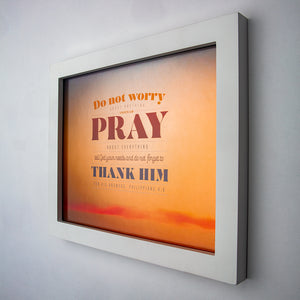 Philippians 4:6 printed in modern fonts and sunset background on fine art paper in white frame.